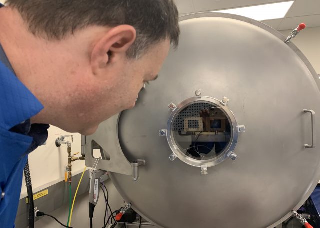 Principal Investigator Jim Bell looking into the vacuum chamber at Malin Space Science Systems, where the flight cameras were tested. The front surfaces of both cameras are visible behind the vacuum chamber window.